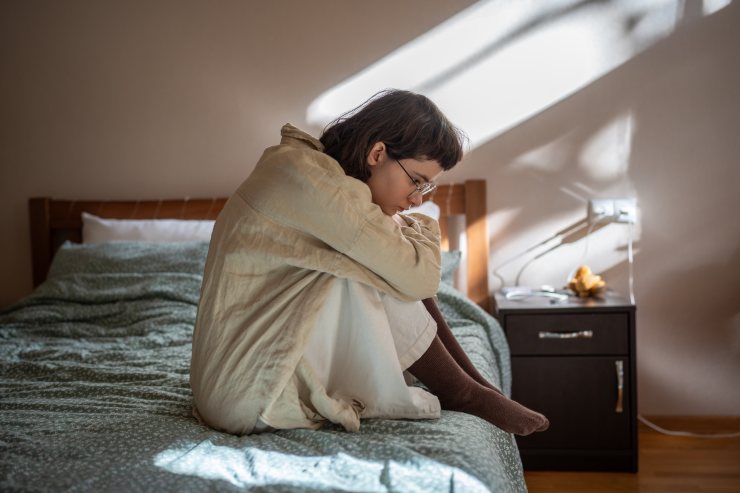 ragazza rannicchiata sul letto: tristezza